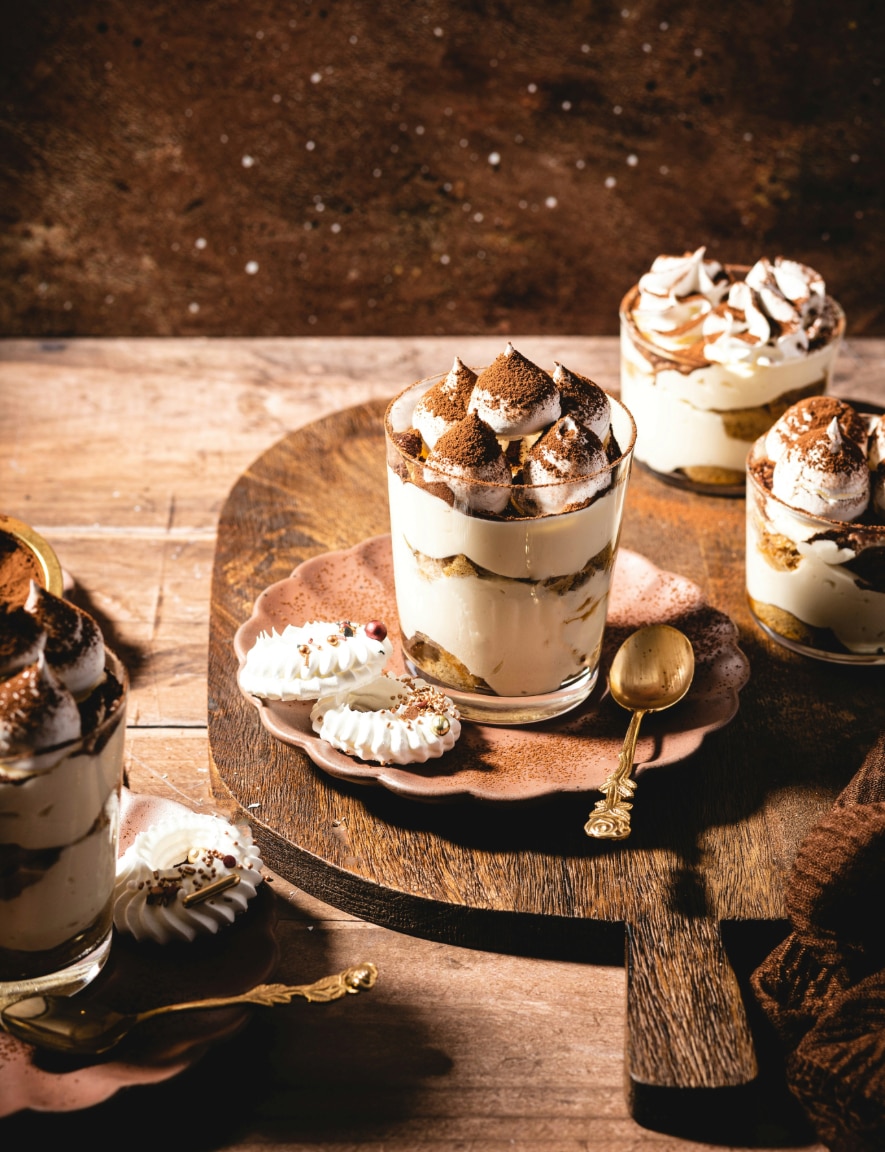 Multiple glasses filled with tiramisu on a wooden board