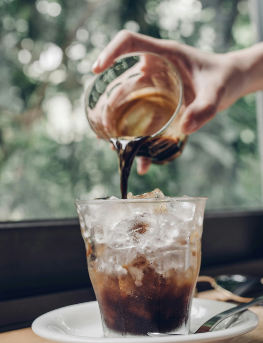 A hand pouring cold coffee into a glass filled with ice