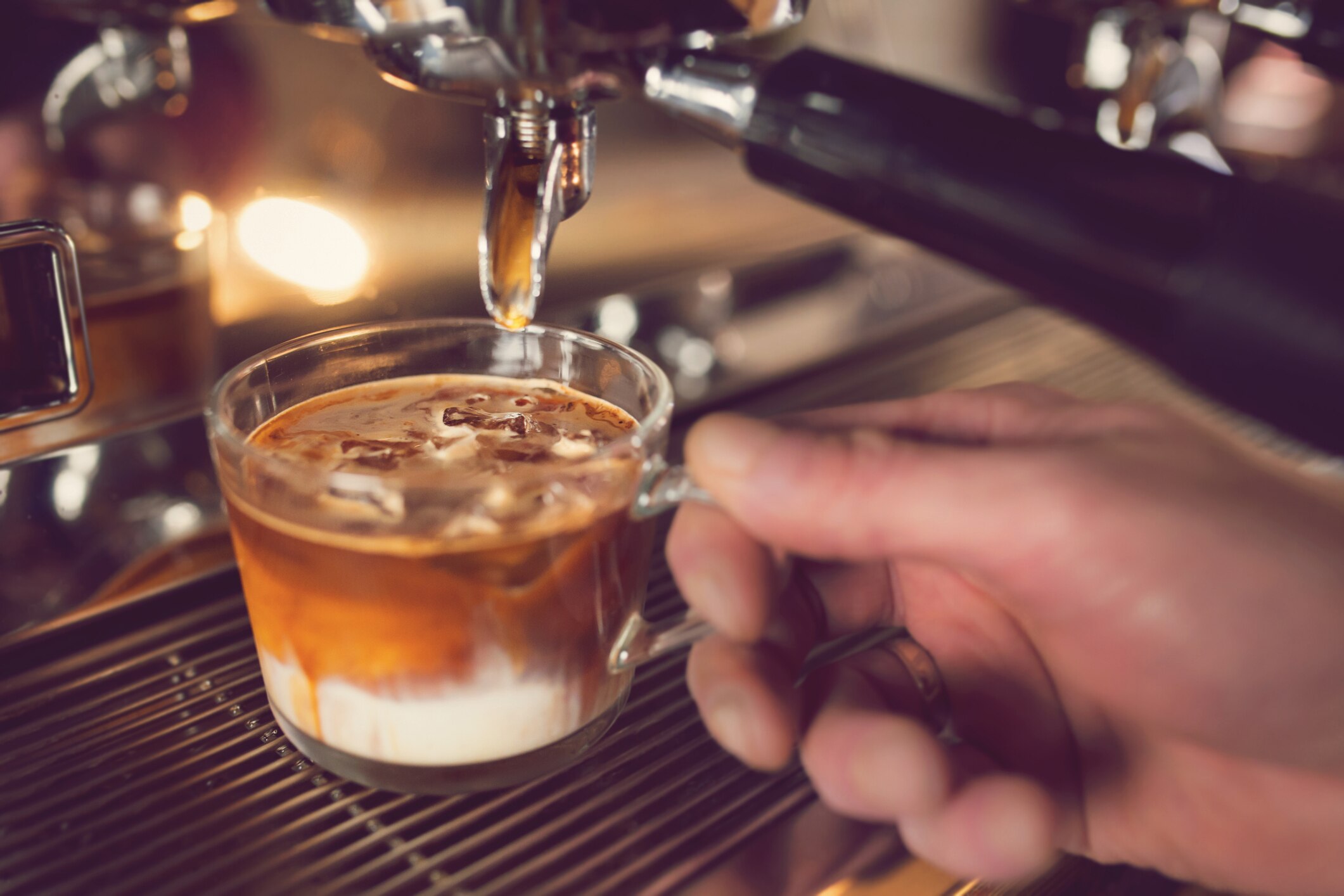 A macchiato being brewed by a barista in a glass mug