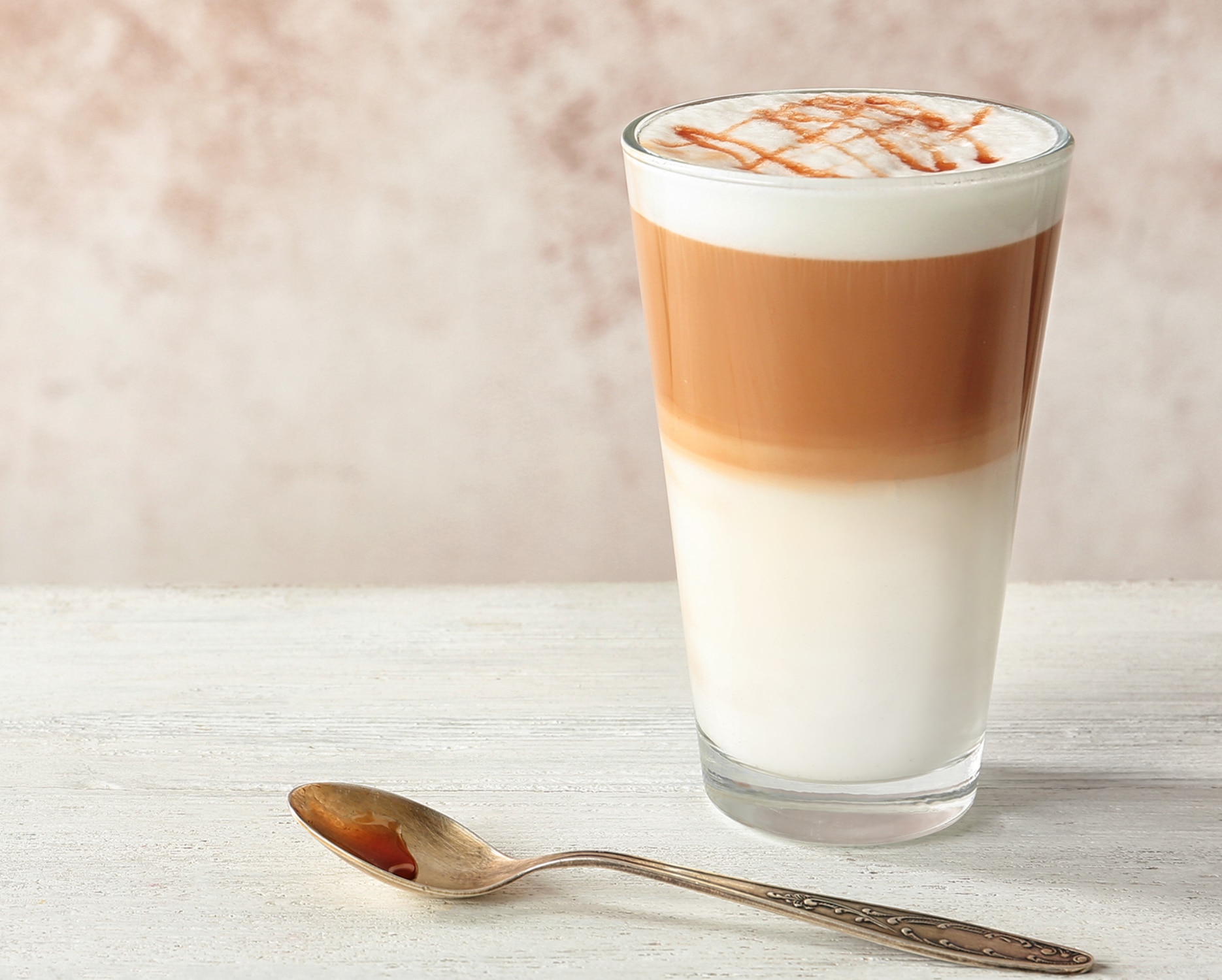 A Caramel Macchiato in a glass on a counter with a spoon in front of it