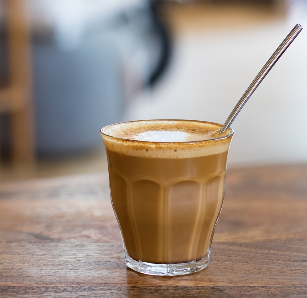 A cortado in a glass on a green saucer