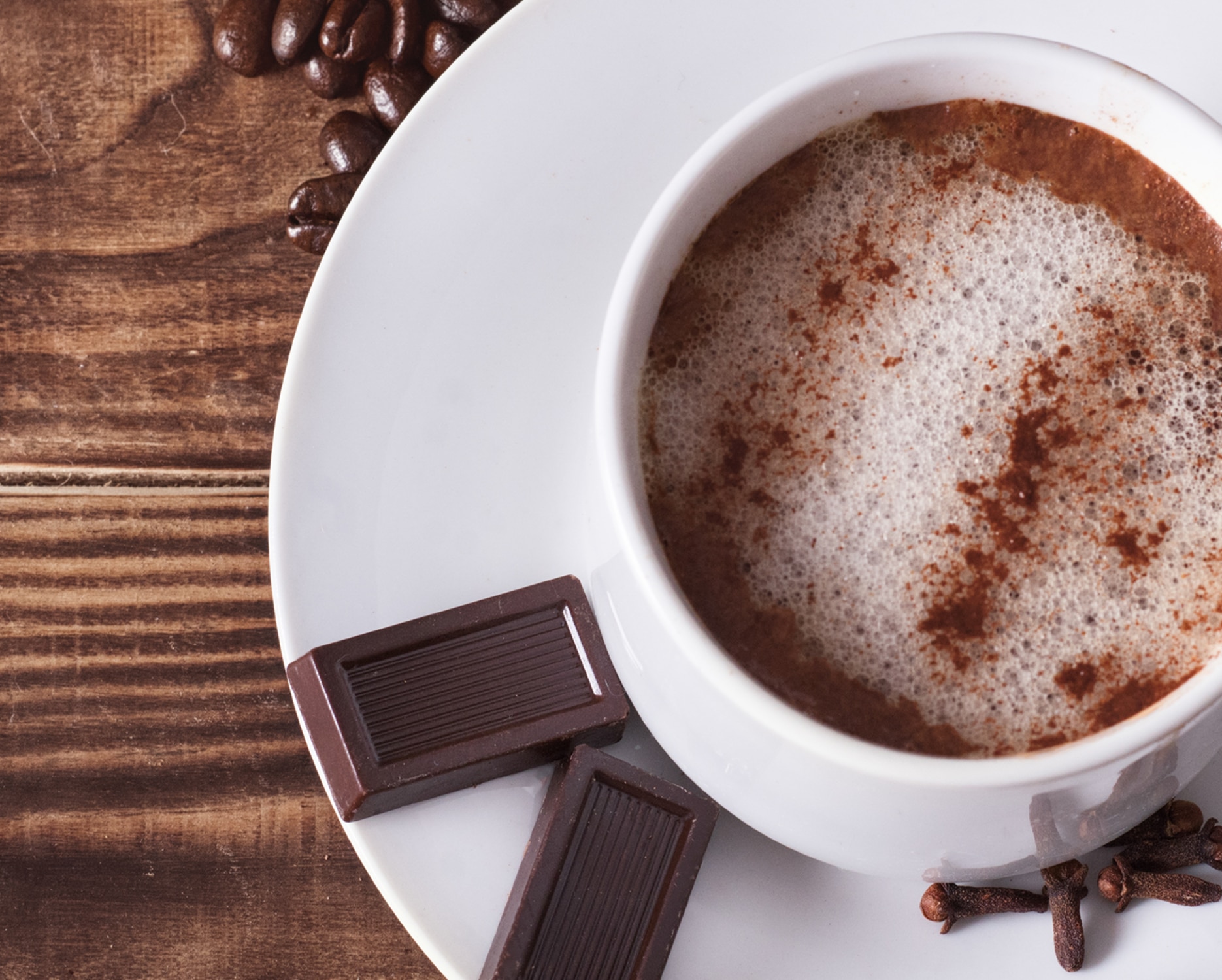 A Mocha in a white cup on a small plate with chocolate next to it